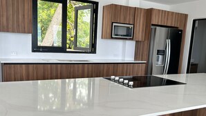 A modern kitchen with a central island, wooden cabinets, a built-in microwave, and a stainless steel refrigerator.