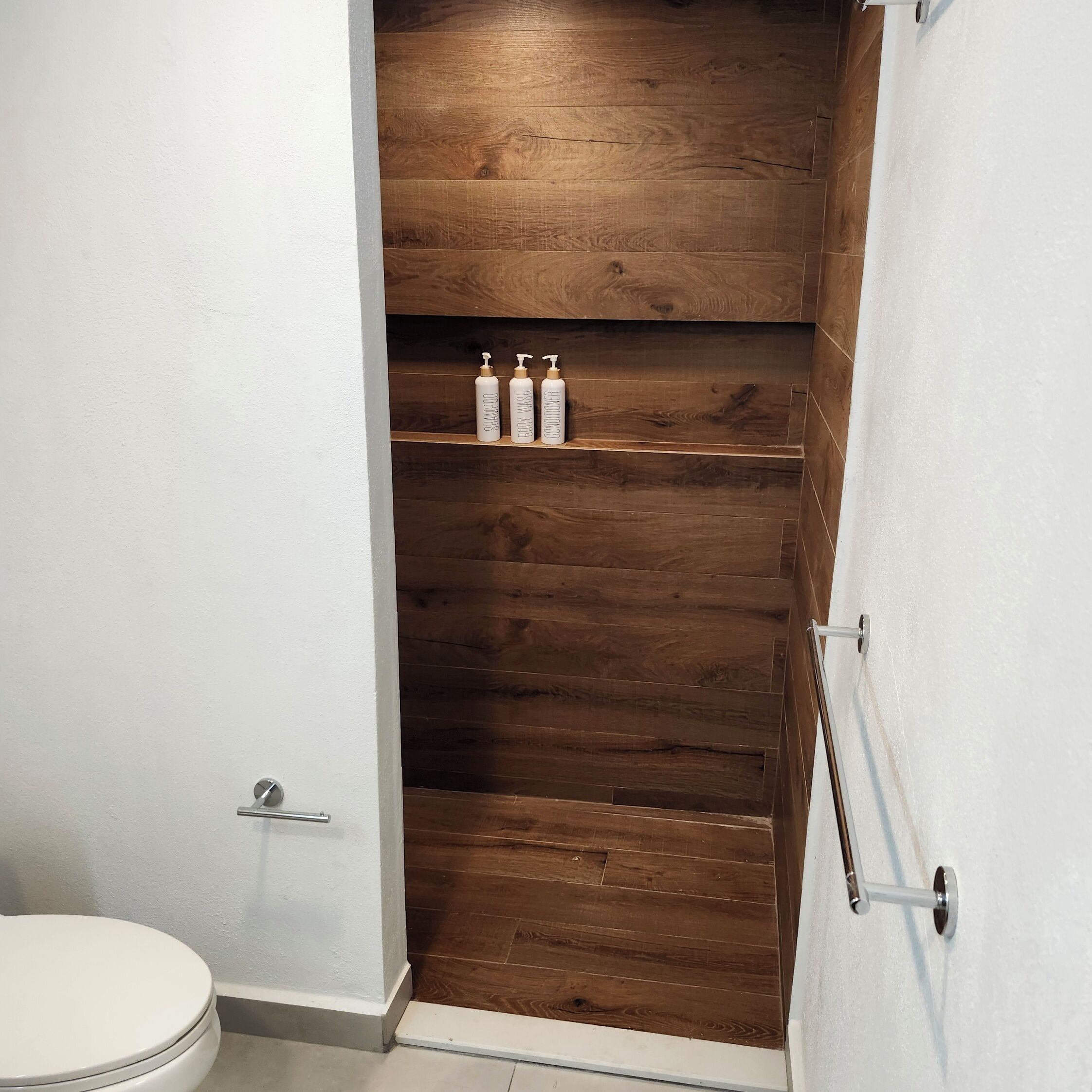 A bathroom with a wooden vanity, a toilet, and three bottles of shampoo on the vanity.