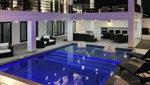 A modern two-story house with a swimming pool, outdoor seating, and a balcony.