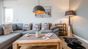 A modern living room with a grey sofa, a wooden coffee table, and a painting of a snowy beach scene.