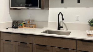 Een moderne keuken met houten kastjes, een roestvrijstalen magnetron, een zwarte kraan en een aanrecht met een broodrooster en glazen potten.