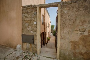 A narrow alleyway with stone walls, a metal gate, and a staircase leading to a building.