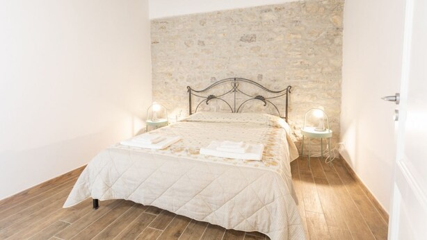 Ein Schlafzimmer mit Stehwand, einem Bett mit Tagesdecke, zwei Nachttischen mit Lampen und Holzboden.
