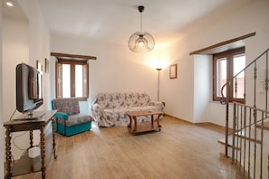 Una sala de estar con un sofá, televisión, mesa y una escalera.