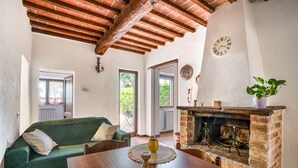 A cozy living room with a green sofa, wooden dining table, and a brick fireplace. - GuestHost - Elegant 85 sqm apartment in a renovated farmhouse in Castiglione del Lago, Umbria. Ideal for 4 people, it offers a communal pool, a reserved outdoor parking space for guests, and a private garden. Surrounded by nature, it is perfect for those (Castiglione del Lago)
