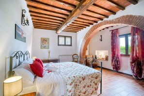 A bedroom with a bed, a window, a radiator, and an arched brick ceiling.