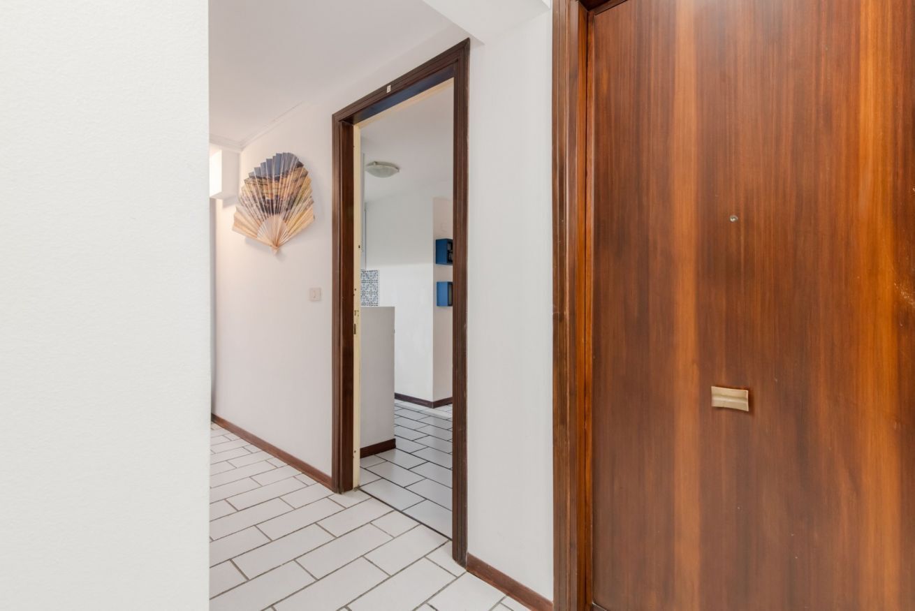 A hallway with a wooden door, a white wall, and a tiled floor.