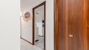 Een gang met een houten deur, een witte muur en een betegelde vloer.
