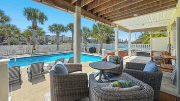 A covered outdoor area with wicker furniture, a pool, and a view of palm trees and buildings.