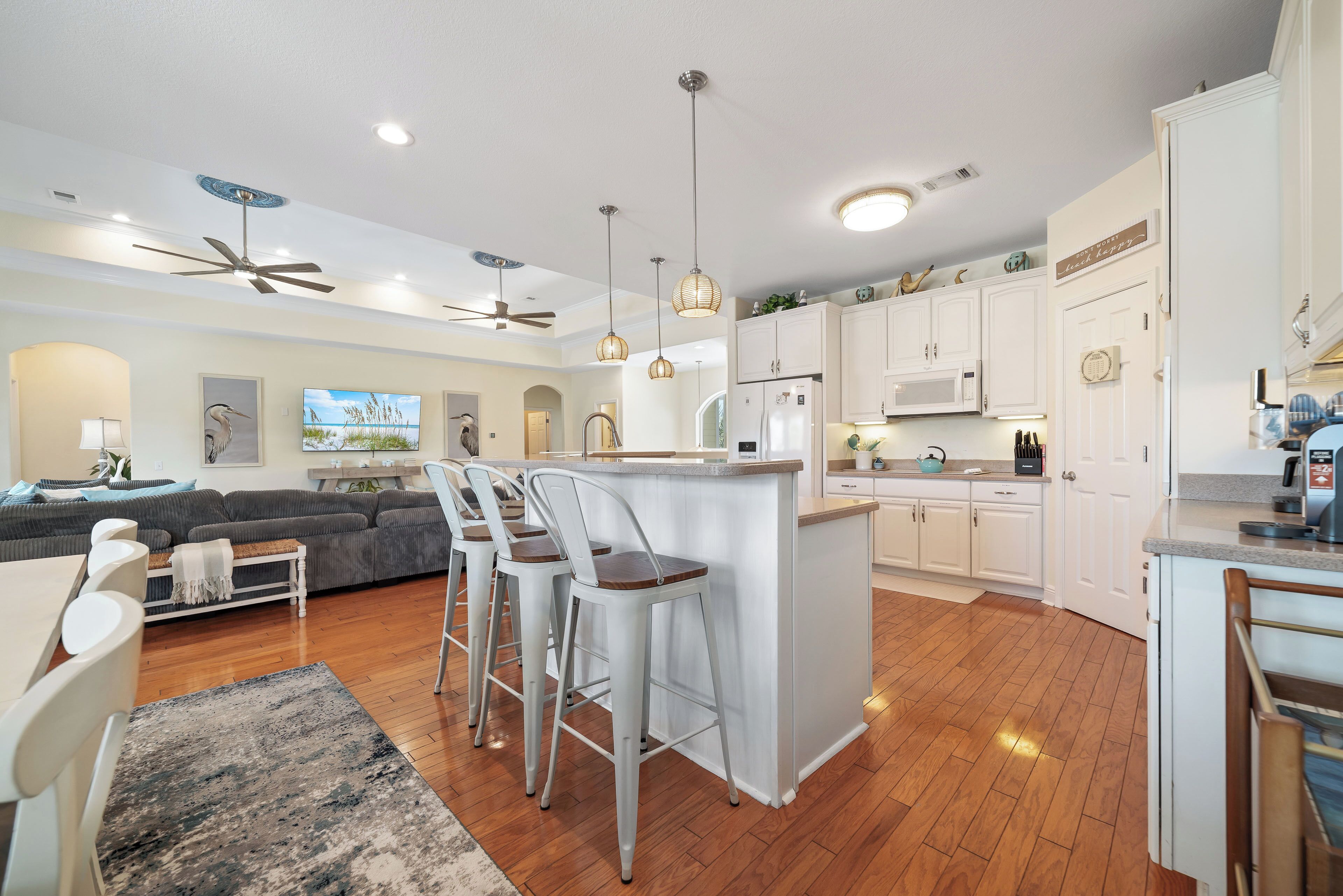 A modern kitchen with white cabinets, a central island, bar stools, and a ceiling fan.