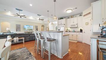 A modern kitchen with white cabinets, a central island, bar stools, and a ceiling fan.
