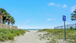 A sandy beach path with a sign for 'Snorkel Reef' and a wooden fence on the left.