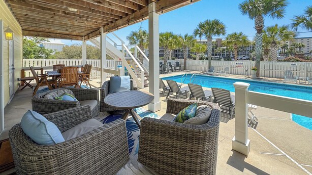 A covered outdoor area with wicker furniture, a pool, and palm trees.