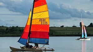 A sailboat with a multicolored sail on a calm body of water.