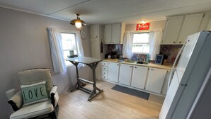 A compact kitchen with a dining table, a chair with a cushion, a refrigerator, and a window with curtains.