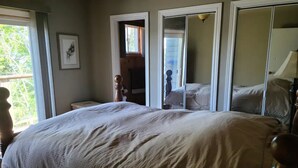 A bedroom with a large bed, a wooden headboard, a window with curtains, a framed picture on the wall, and a door leading to another room. - Feathery Pines cottage with sauna and sunset views (Nobel)