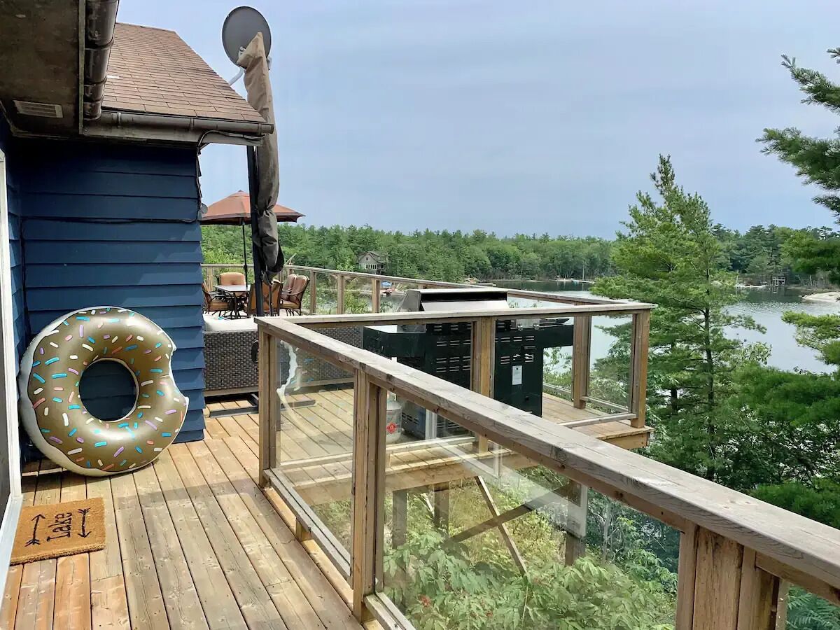 A wooden deck with a view of a lake and trees, a satellite dish, and a donut-shaped inflatable ring.