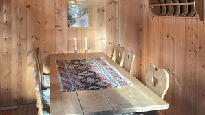 Puisesta valmistettu ruokapöytä, jonka päällä on kuvioitu pöytäliina, kynttilöitä ja maalaishenkinen kattokruunu.