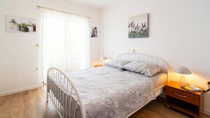 Et soveværelse med seng, sengeborde, lampe, gardiner ved et vindue samt billedkunst på væggen.