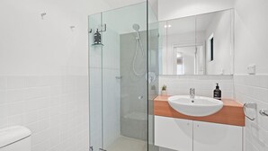 A modern bathroom with a glass shower enclosure, a white sink with a wooden countertop, and a large mirror above the sink.