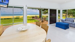 Sala moderna com uma grande porta de vidro que dá para a praia, mesa de jantar redonda, cadeiras de vime e sofá listrado.