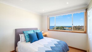 Une chambre à coucher avec un lit, des oreillers, une table de chevet et une fenêtre donnant sur la mer et le paysage.