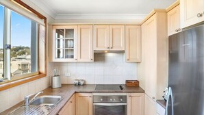 Une cuisine moderne avec des meubles en bois clair, un réfrigérateur en acier inoxydable, un four encastré et une fenêtre offrant une vue sur la ville.