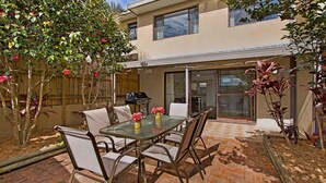 Eine Terrasse mit einem Glastisch und Stühlen, umgeben von Pflanzen und einem Holzzaun.