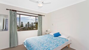 Ein Schlafzimmer mit Bett, Nachttisch, Fenster mit Vorhängen und Deckenventilator.