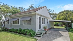 Une maison de plain-pied avec un toit en tuiles, une véranda et un petit jardin devant, agrémenté d’un banc et de plantes en pot.