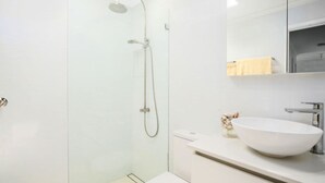 A modern bathroom with a large white sink, a glass shower enclosure, and a mirror above the sink.