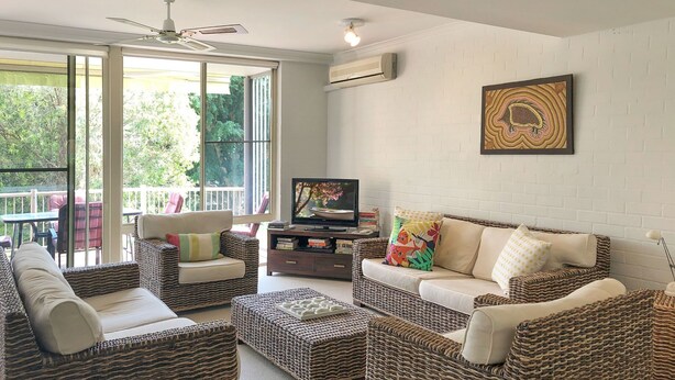 A living room with wicker furniture, a television, and a large window with a view of greenery.