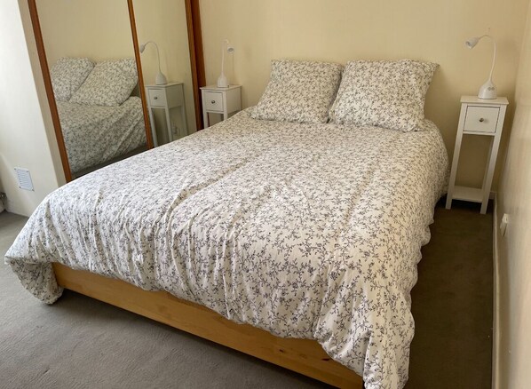 A neatly made bed with a floral bedspread, two bedside tables with lamps, and a mirror on the wall. - Beautiful house with garden and attic between Marché aux Puces and La Communale (Saint-Ouen-sur-Seine)