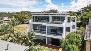 A modern two-story building with large glass windows, a flat roof, and a balcony. - Avoca Views (Avoca Beach)