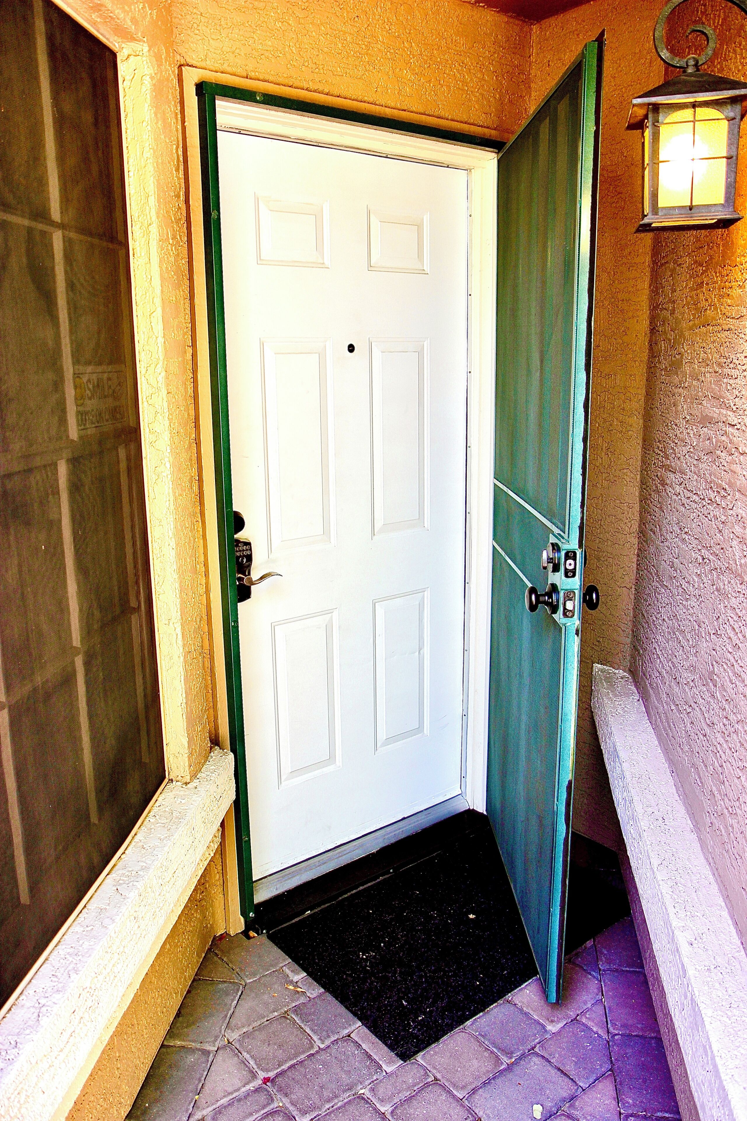 A white door with a green frame, a black doormat, and a wall-mounted light fixture.