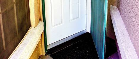 A white door with a green frame, a black doormat, and a wall-mounted light fixture.