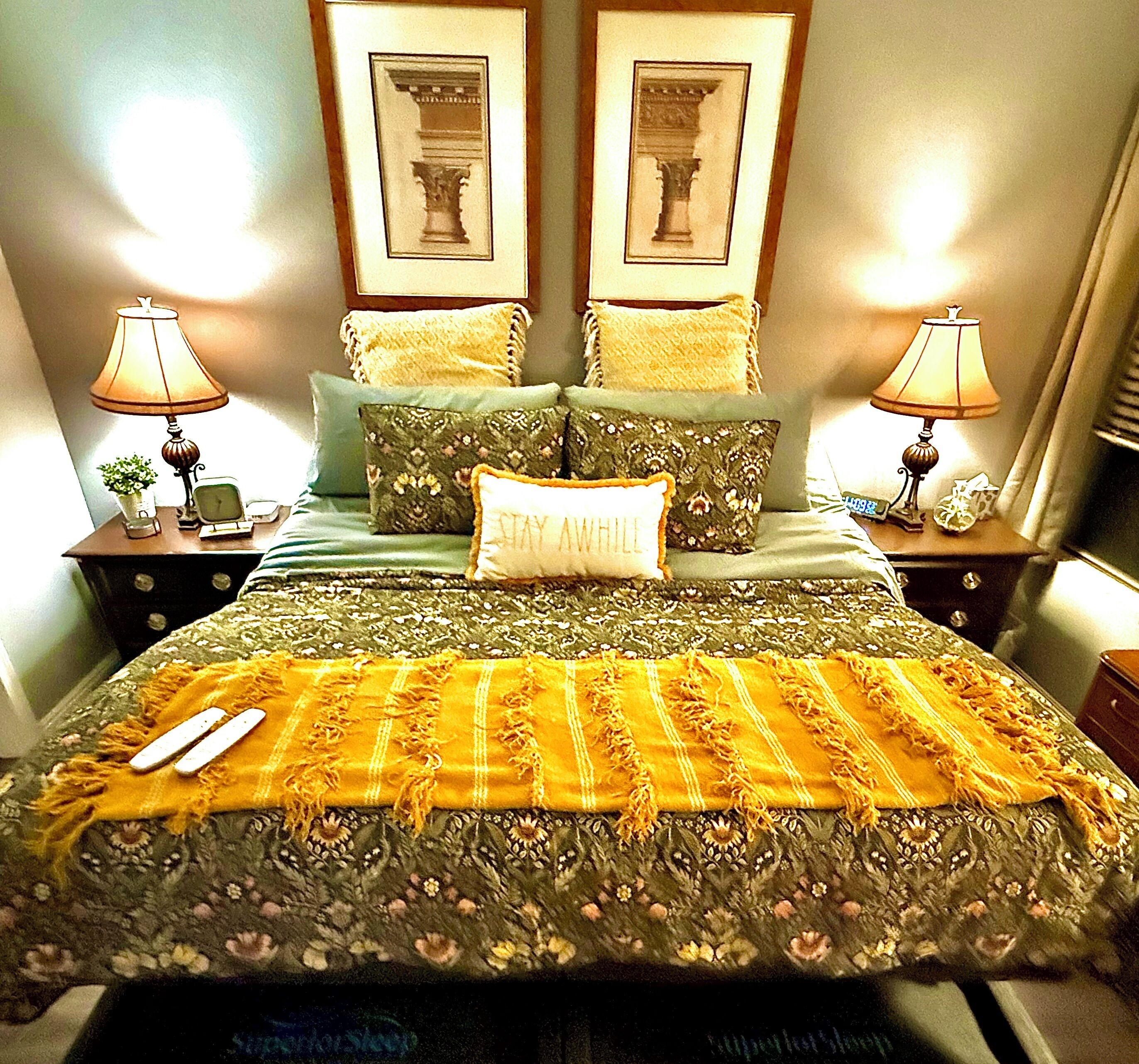 A neatly made bed with floral bedding, two framed pictures on the wall, and bedside lamps.