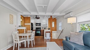 Una cocina moderna con armarios blancos, un refrigerador negro y un microondas. Hay un comedor con sillas blancas y una mesa, y un sofá azul en la sala de estar.