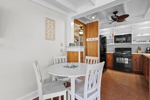 A modern kitchen with white cabinetry, a black refrigerator, a microwave, and a stove. There is a dining table with white chairs.
