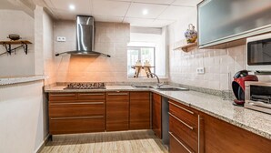 Uma cozinha moderna com coifa de aço inoxidável, bancadas de granito, armários de madeira, forno embutido e uma janela que oferece iluminação natural.