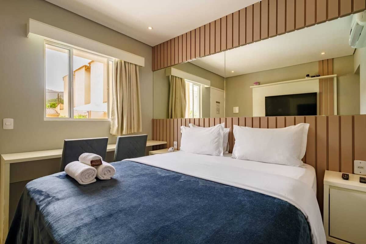 A hotel room with a bed, a desk, a chair, a TV, and a window with curtains.