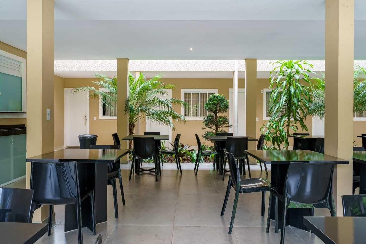 Un amplio comedor interior con varias mesas y sillas, rodeado de plantas en macetas y un techo con diseño.