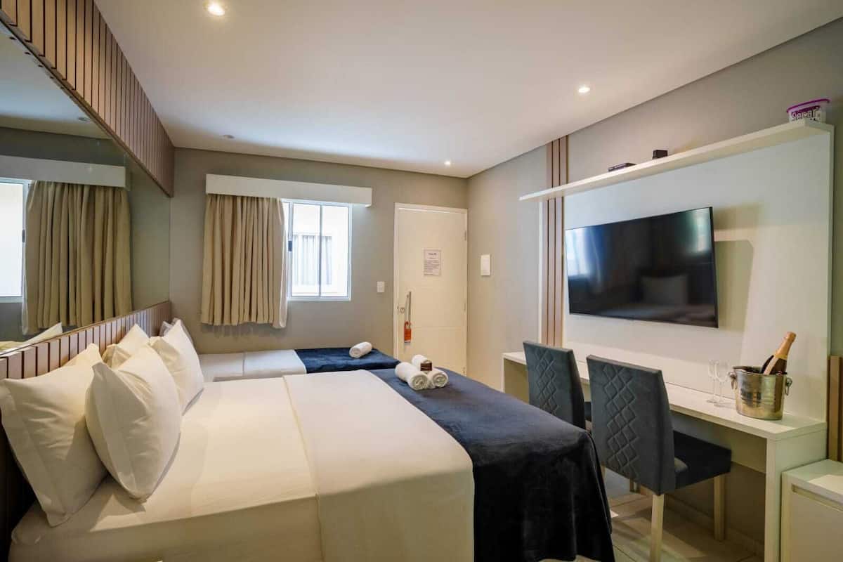 A hotel room with a large bed, a desk with a chair, a television, and a minibar.