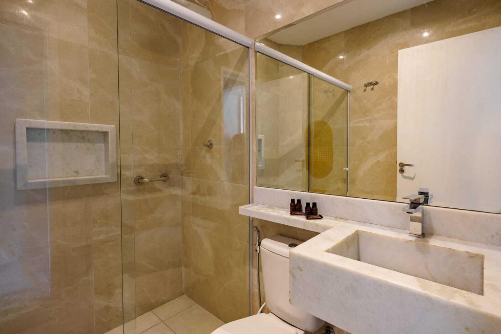 Un baño moderno con ducha de vidrio, tocador de mármol y un espejo grande.