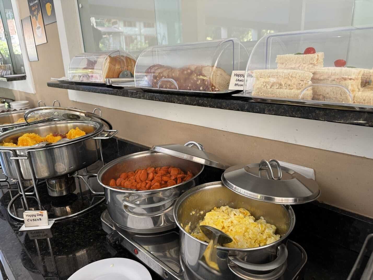 A buffet with various food items including scrambled eggs, carrots, and sandwiches.