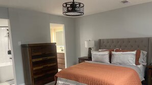 A bedroom with a large bed, a wooden dresser, and a modern pendant light. - End unit townhome with side yard (Baton Rouge)