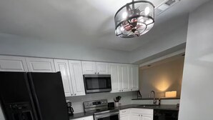 A modern kitchen with white cabinets, stainless steel appliances, and a grey herringbone floor. - End unit townhome with side yard (Baton Rouge)