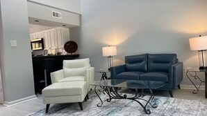 A modern living room with a white armchair, a blue sofa, and a glass coffee table. - End unit townhome with side yard (Baton Rouge)