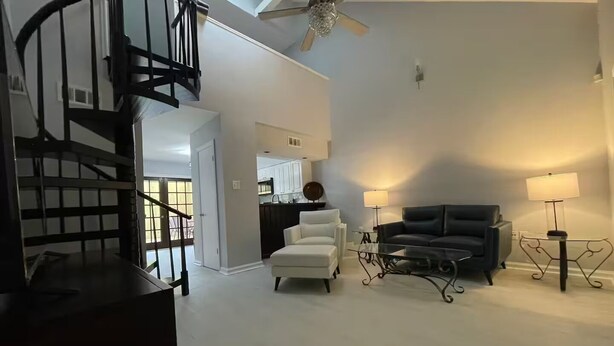 A spacious living area with a modern staircase, a black leather sofa, a white armchair, and a glass coffee table. - End unit townhome with side yard (Baton Rouge)