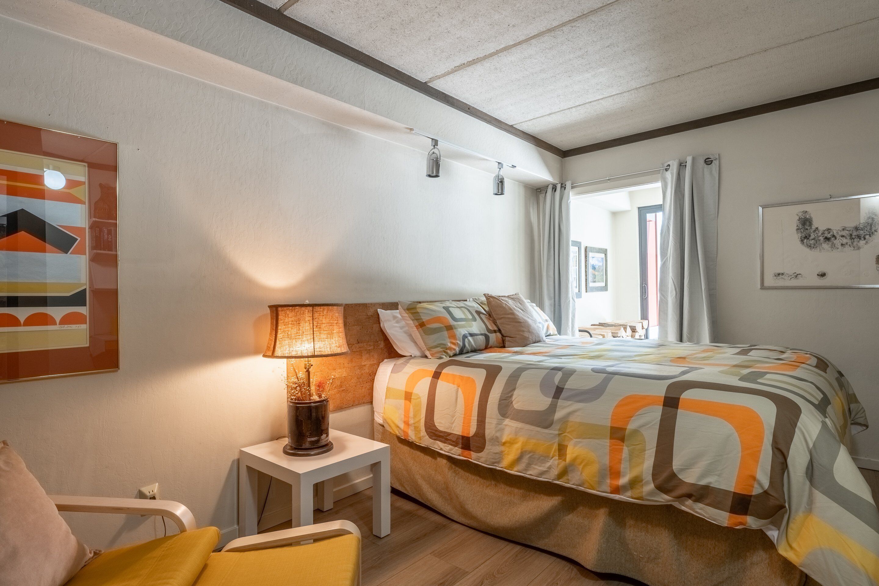 Un dormitorio con cama, mesita de noche, lámpara y un cuadro en la pared.